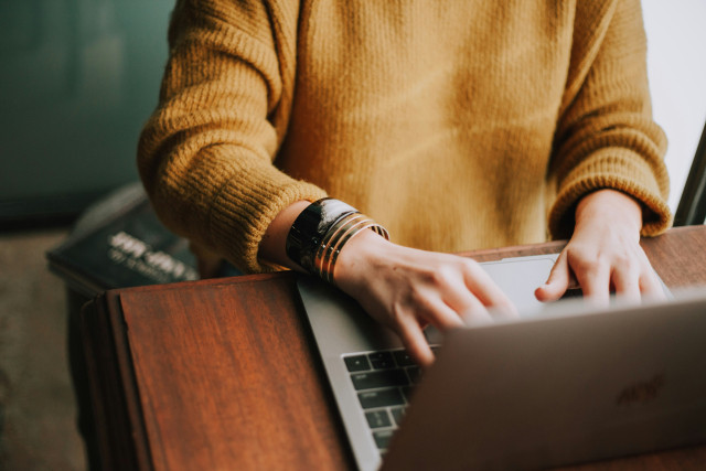 Person sitzt vor Laptop und tippt auf der Tastatur.